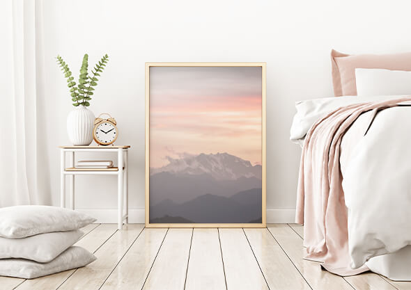 Minimalistic bedroom with light interior and wood floor, showing a bedside table with decorative items on top, a large,   photo frame and a bed with white and light pink bedding on the right